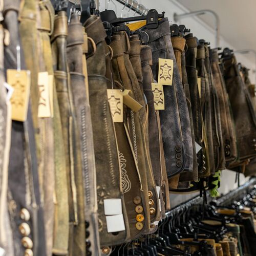 Nahaufnahme von braunen und grauen Lederhosen in verschiedenen Designs, ordentlich auf Kleiderstangen gehängt