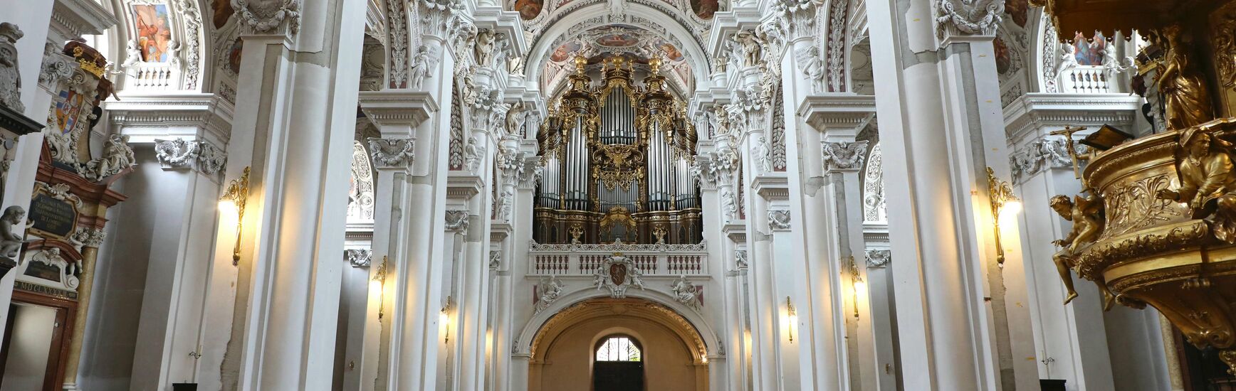 Zentralperspektive auf die imposante Domorgel mit vergoldeten Details im barocken Innenraum des Passauer Stephansdoms.