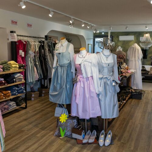 Innenbereich des Trachtenladens mit Dirndl in Rosa, Blau und Fliederfarben auf Puppen vor Holzregalen mit Kleidung