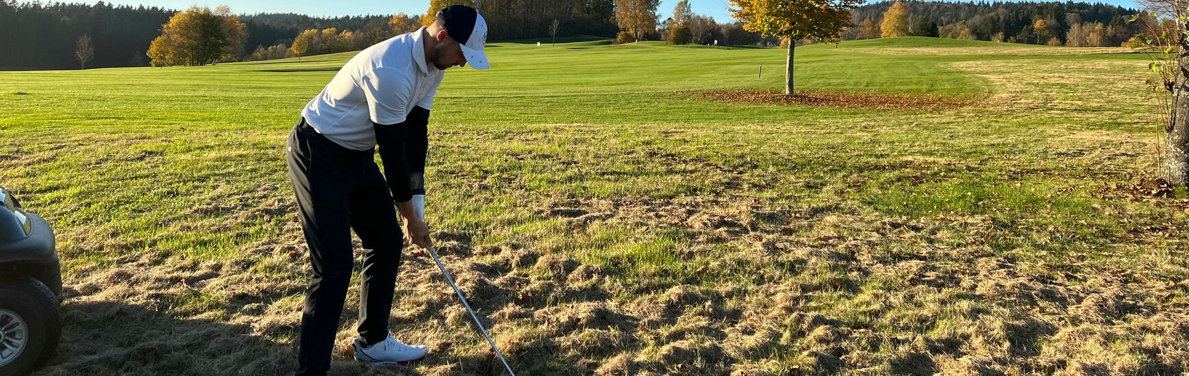 Golfer im herbstlichen Licht bei spätem Abschlag – Bäume teils schon mit buntem Laub.