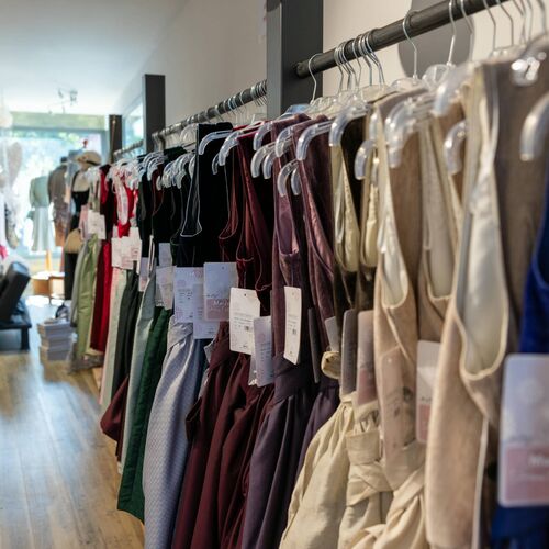 Dirndlkleider in Tönen wie Bordeaux, Grün und Beige auf Kleiderbügeln entlang einer Wand im Innenraum