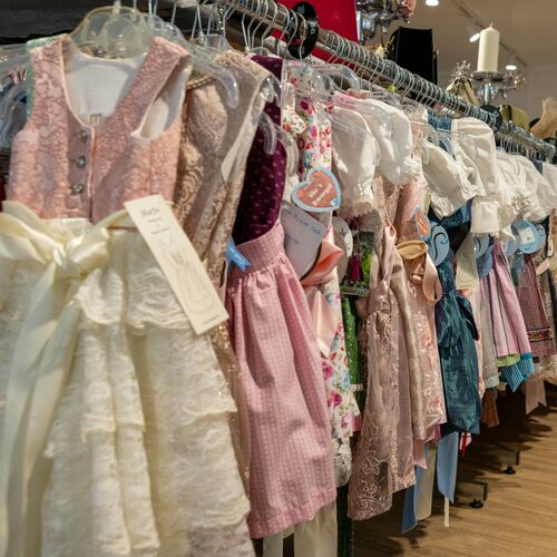Bunte Kinderdirndl in Pastell- und Trachtenfarben auf Kleiderstangen in einem traditionellen Modegeschäft